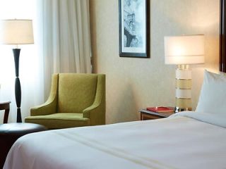 A hotel room with a plush white bed and green armchair, complemented by soft lighting and elegant decor.